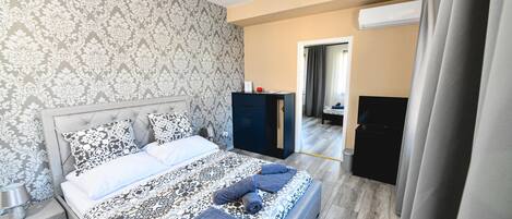 A bedroom with a patterned bedspread, a nightstand, a dresser, and a door leading to another room.