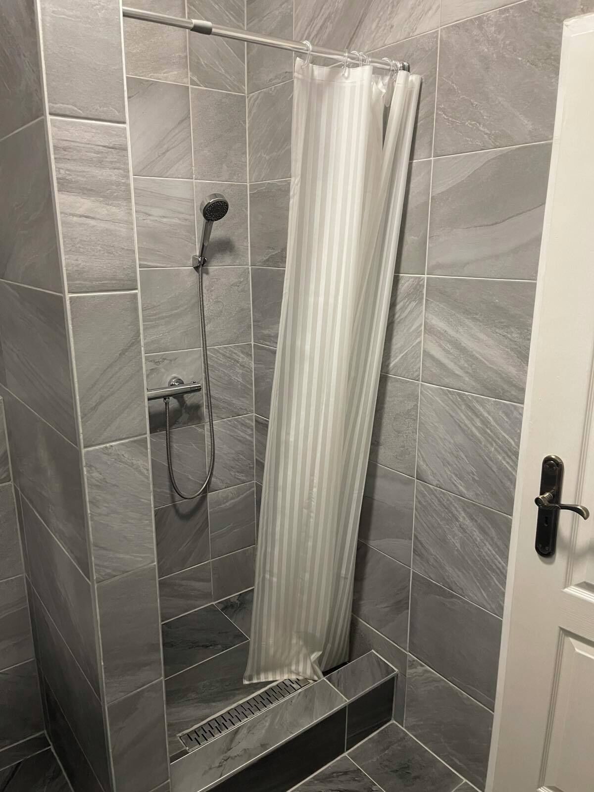 Una ducha a pie con puerta de cristal, azulejos de mármol gris y un cabezal de ducha.