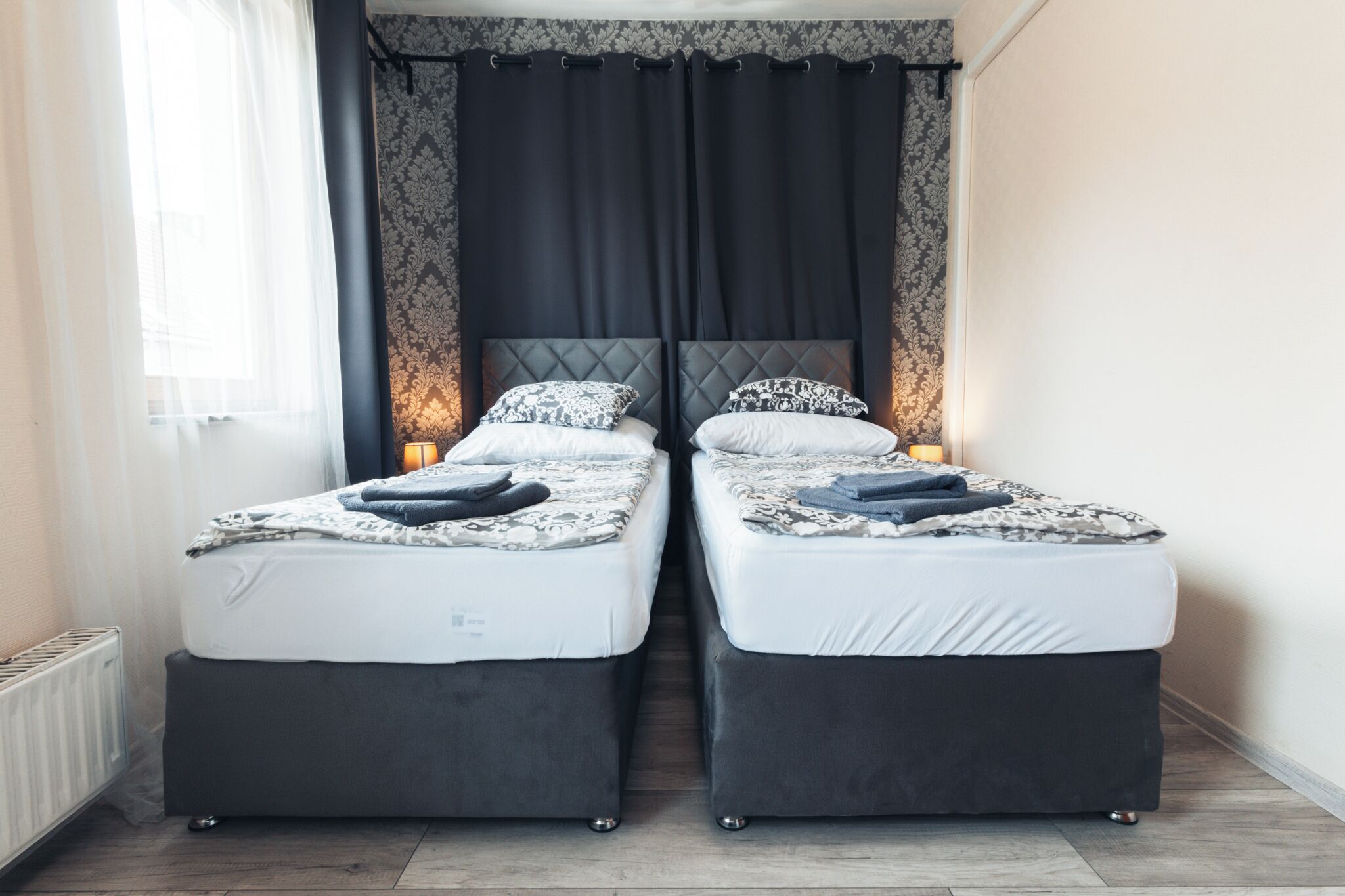 A twin room with two beds, a radiator, and a window with sheer curtains.