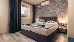 A modern bedroom with a large bed, a bedside table with a lamp, and a patterned wallpaper. - Végvári Hotel Eger (Eger)