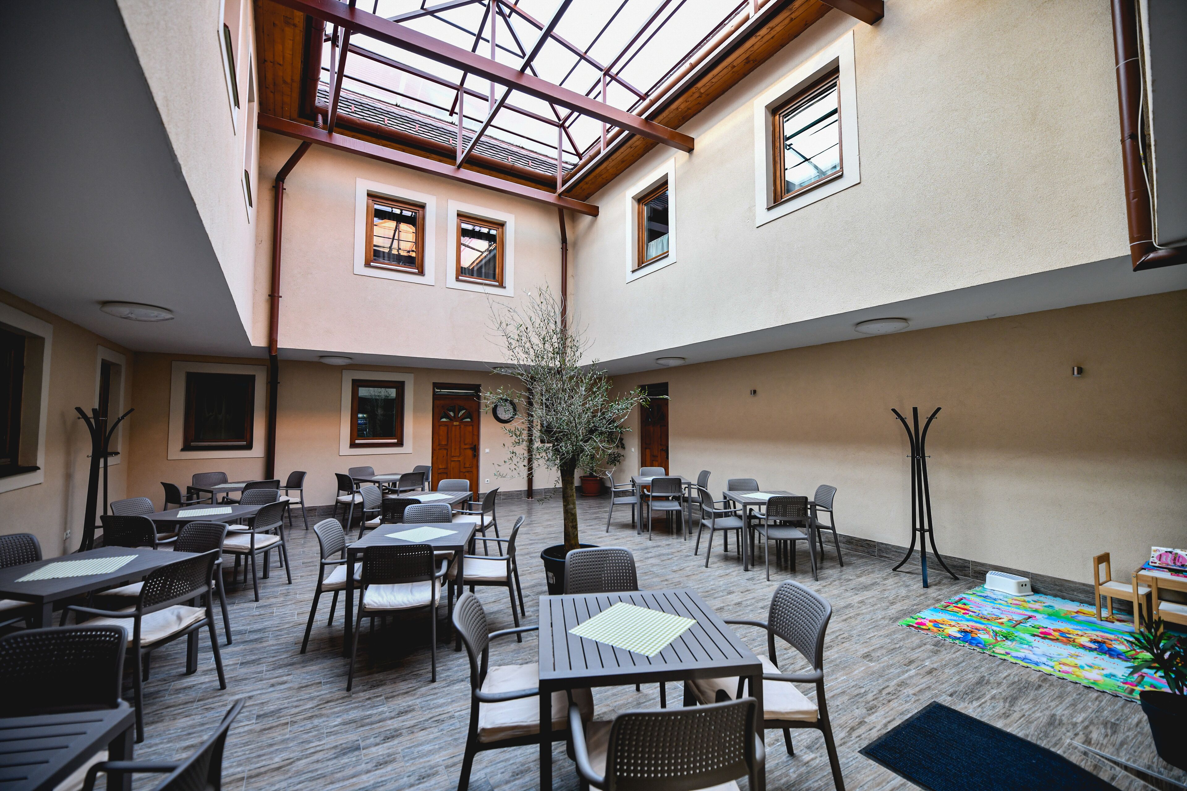 A spacious outdoor dining area with multiple tables and chairs, a central tree, and a colorful rug.
