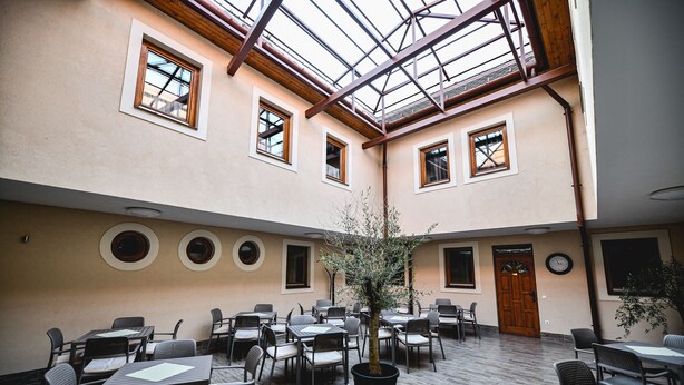 An indoor courtyard with multiple tables and chairs, a central tree, and a wooden door. - Végvári Hotel Eger (Eger)