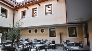 A spacious indoor dining area with multiple tables and chairs, a large potted tree, and a high ceiling with wooden beams. - Végvári Hotel Eger (Eger)