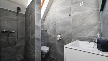 A modern bathroom with grey marble tiles, a shower, a toilet, and a white sink with a soap dispenser.