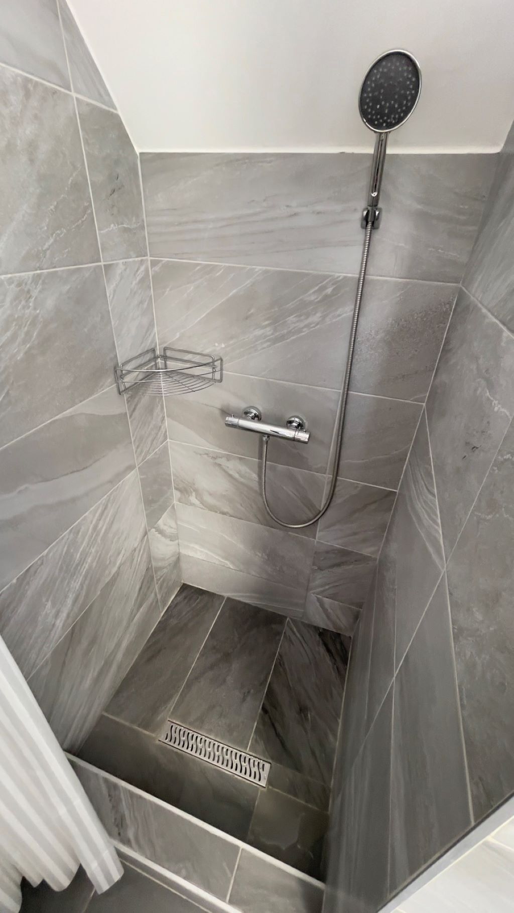 Ducha con cabezal de ducha de mano y panel de control en la pared.