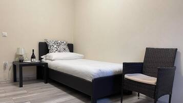 Un dormitorio pequeño y moderno con una cama individual, una mesita de noche con lámpara y una silla de mimbre.