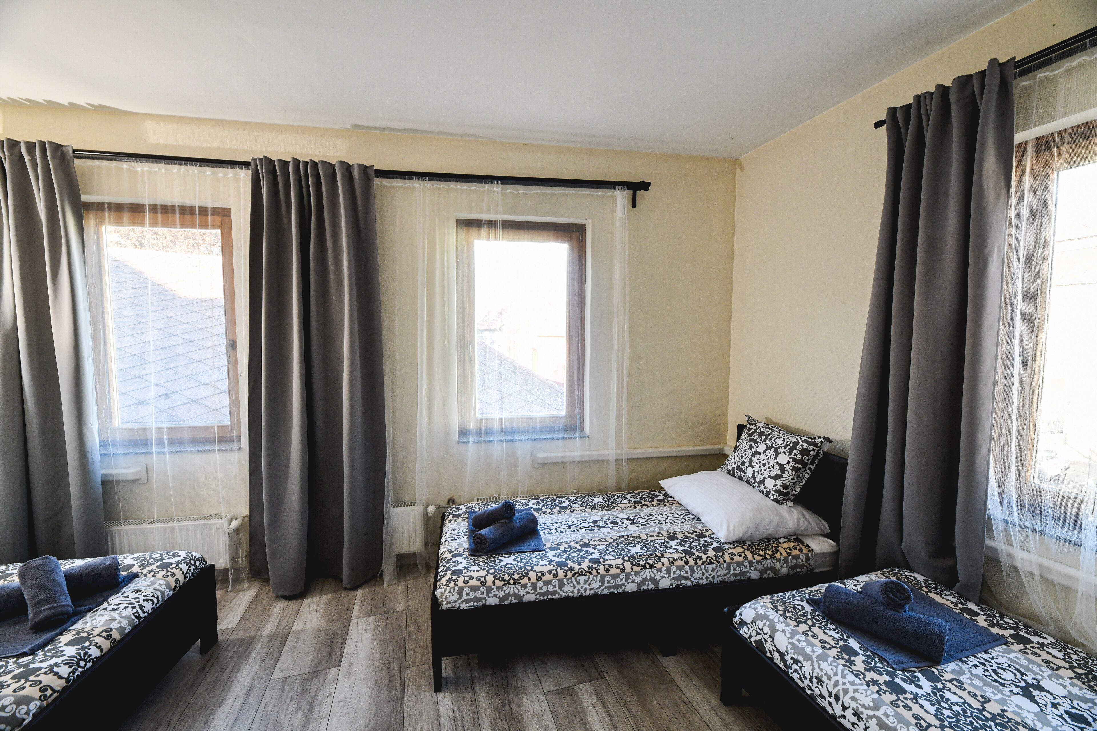 A room with two beds, a window with curtains, and a radiator.