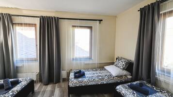 A room with two beds, a window with curtains, and a radiator.