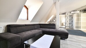 A modern loft bedroom with a large window, a gray sectional sofa, a small table, and a patterned door. - Végvári Hotel Eger (Eger)