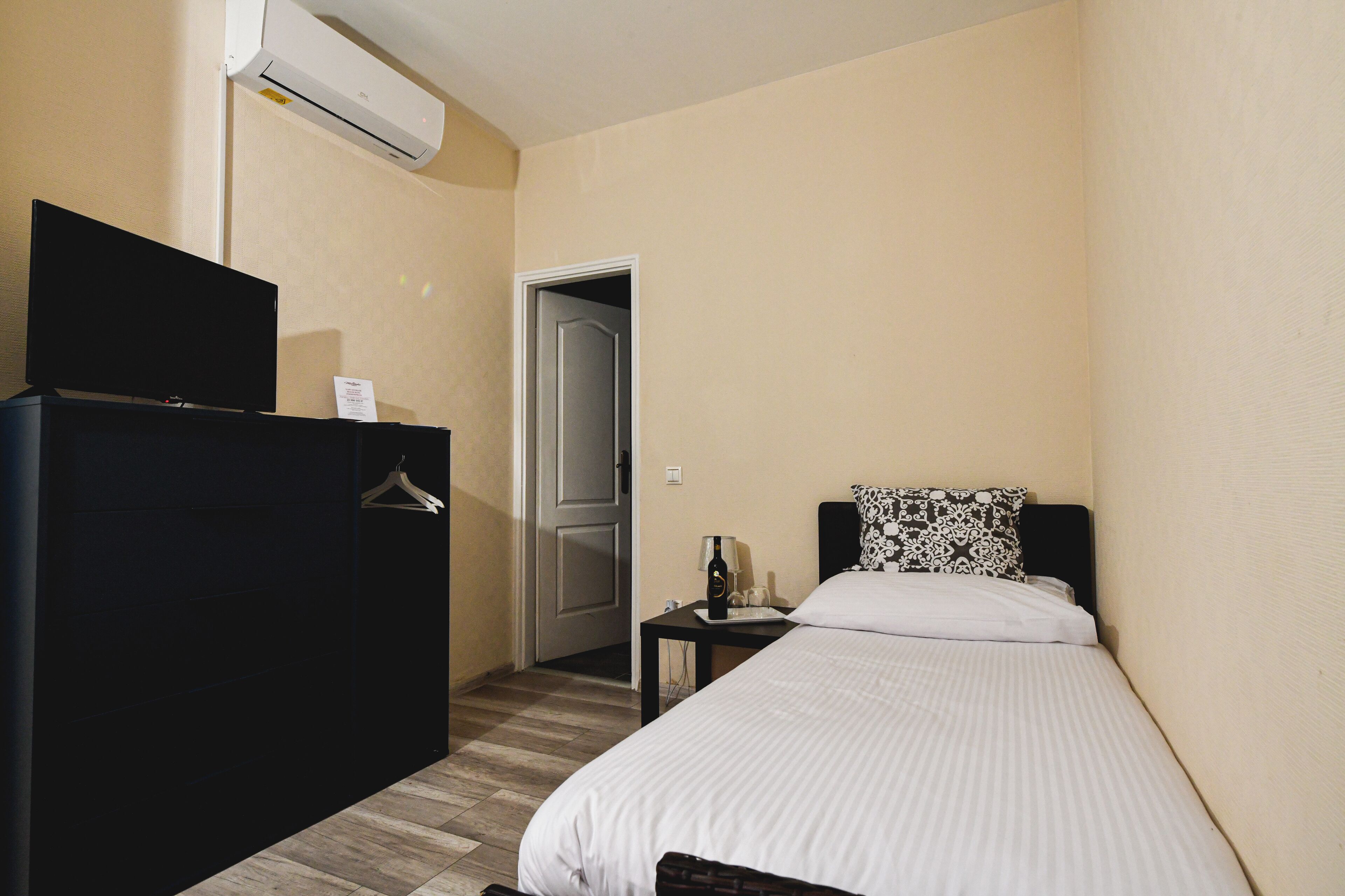 Ein Hotelzimmer mit einem Bett, einem Fernseher auf einer Kommode, einem kleinen Tisch mit einer Flasche und einer Klimaanlage an der Wand.