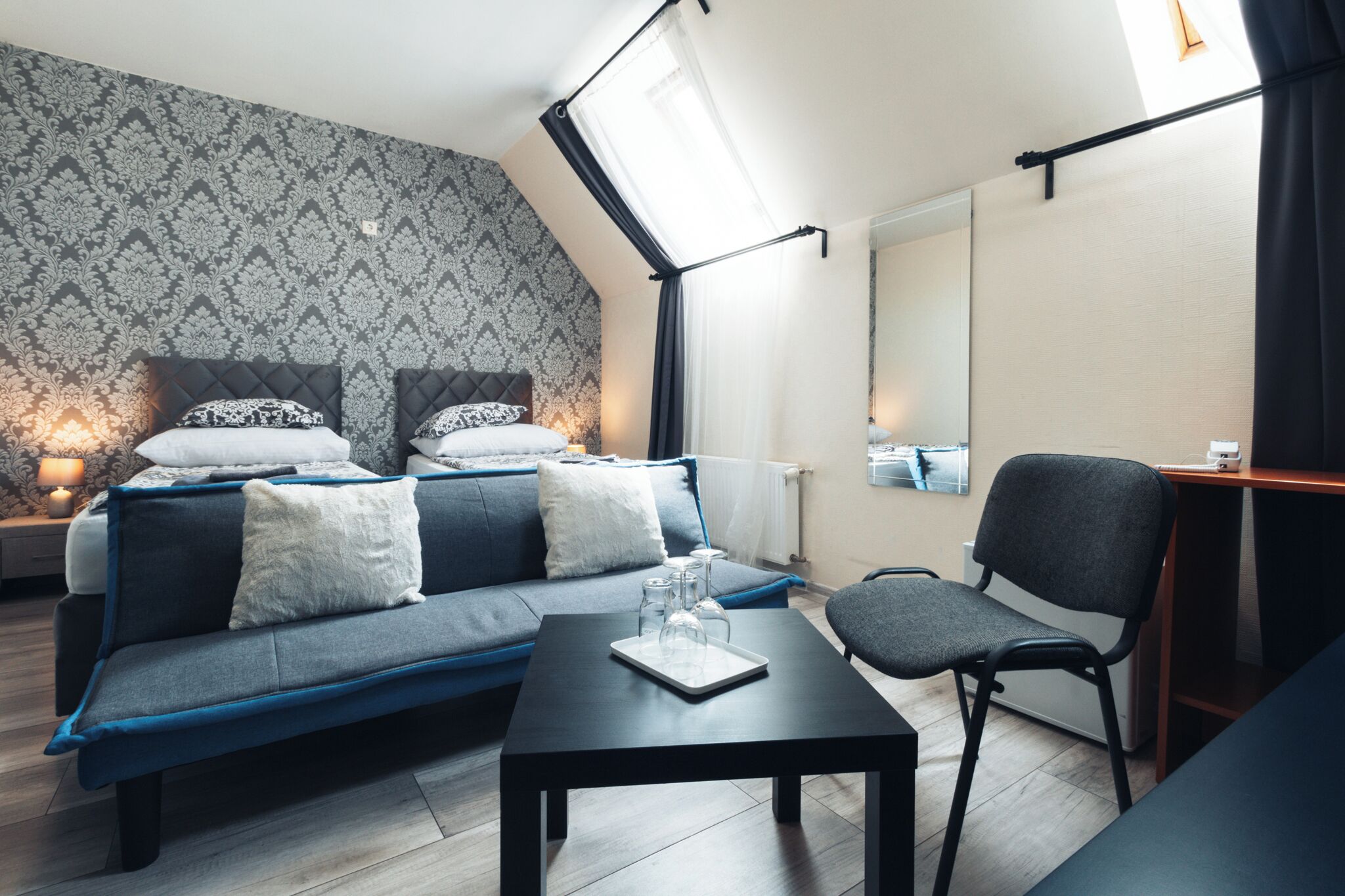 Una habitación de hotel moderna con cama elevada, sofá, una mesita y una silla.