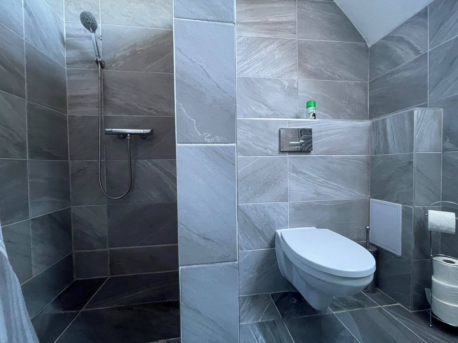 Un baño moderno con baldosas de mármol gris, ducha, inodoro y dispensador de toallas.