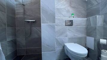 Un baño moderno con baldosas de mármol gris, ducha, inodoro y dispensador de toallas.