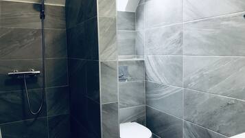 A bathroom with dark grey tiles, a shower with a handheld showerhead, and a toilet.