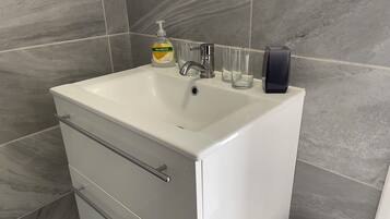 A bathroom with a white sink, a soap dispenser, and three clear glasses.