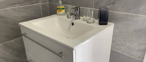 Une salle de bain avec un lavabo blanc, un distributeur de savon et trois verres transparents.