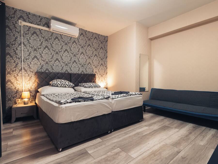 Quarto com cama, mesa de cabeceira, luminária, aparelho de ar condicionado e um sofá.