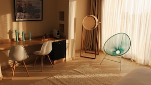 Hotellihuone, jossa on puinen työpöytä, kaksi tuolia, sänky, pyöreä peili ja vihreä tuoli.