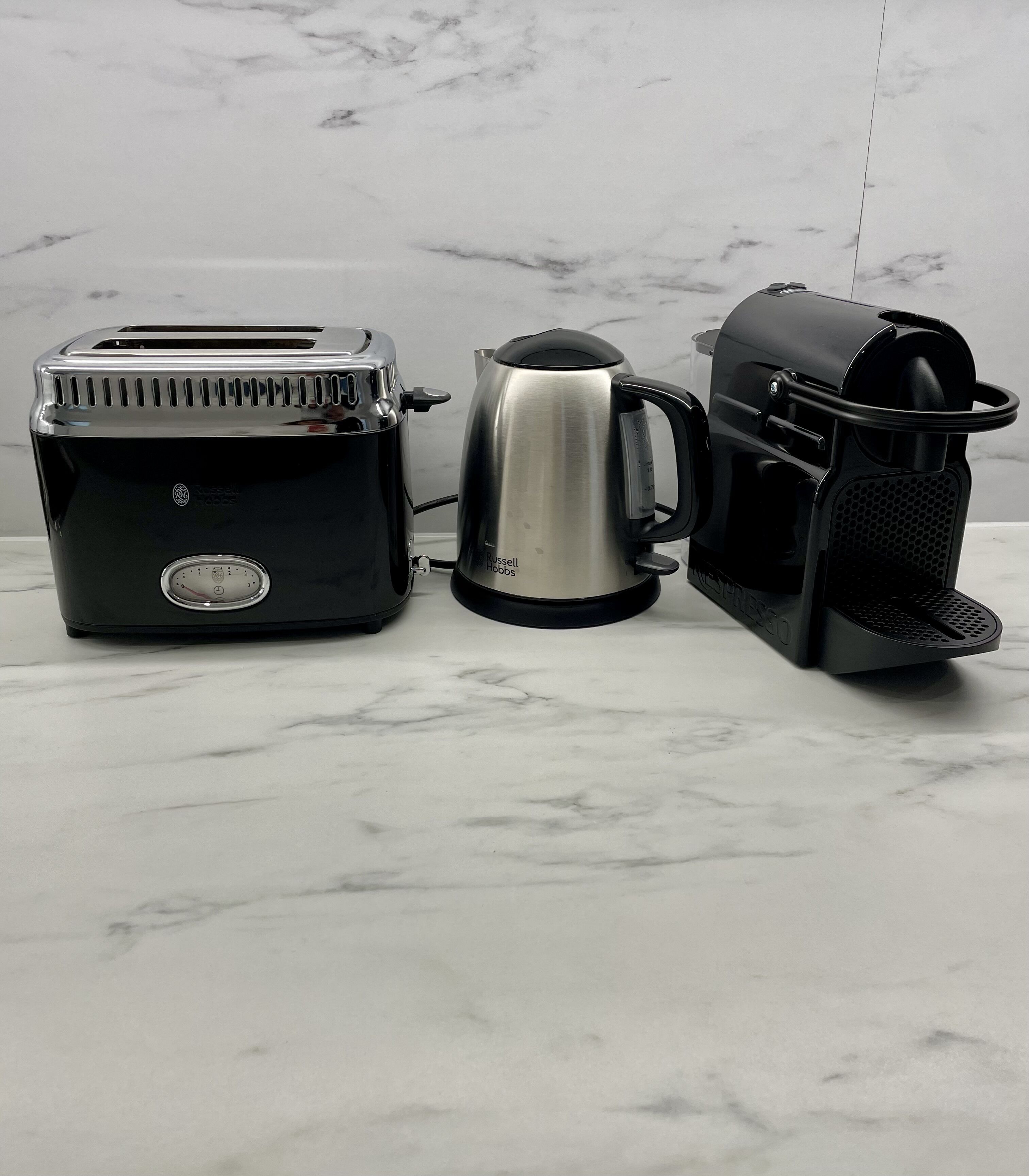 A kitchen with a toaster, a kettle, and a coffee maker on a marble countertop.