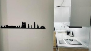 A modern kitchen with a white countertop, a stainless steel trash bin, and a city skyline silhouette decoration on the wall. - Maison Amienoise Élégante (Amiens)