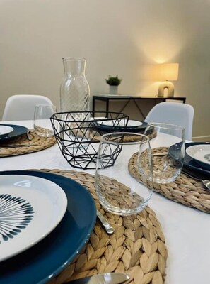 Mesa de comedor dispuesta con cristalería transparente, caminos de mesa tejidos y un centro de mesa geométrico negro.