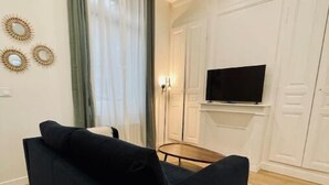 A modern living room with a black sofa, a flat-screen TV mounted on a white wall, and a wooden floor. - Maison Amienoise Élégante (Amiens)