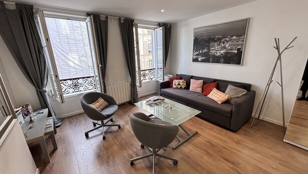A modern living room with a glass coffee table, a sofa with patterned cushions, and a chair. - Charming Apartment in Montmartre (Paris)