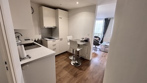 A compact kitchen with white cabinets, a sink, and a bar stool. A dining area with a table and chairs is visible in the background. - Charming Apartment in Montmartre (Paris)