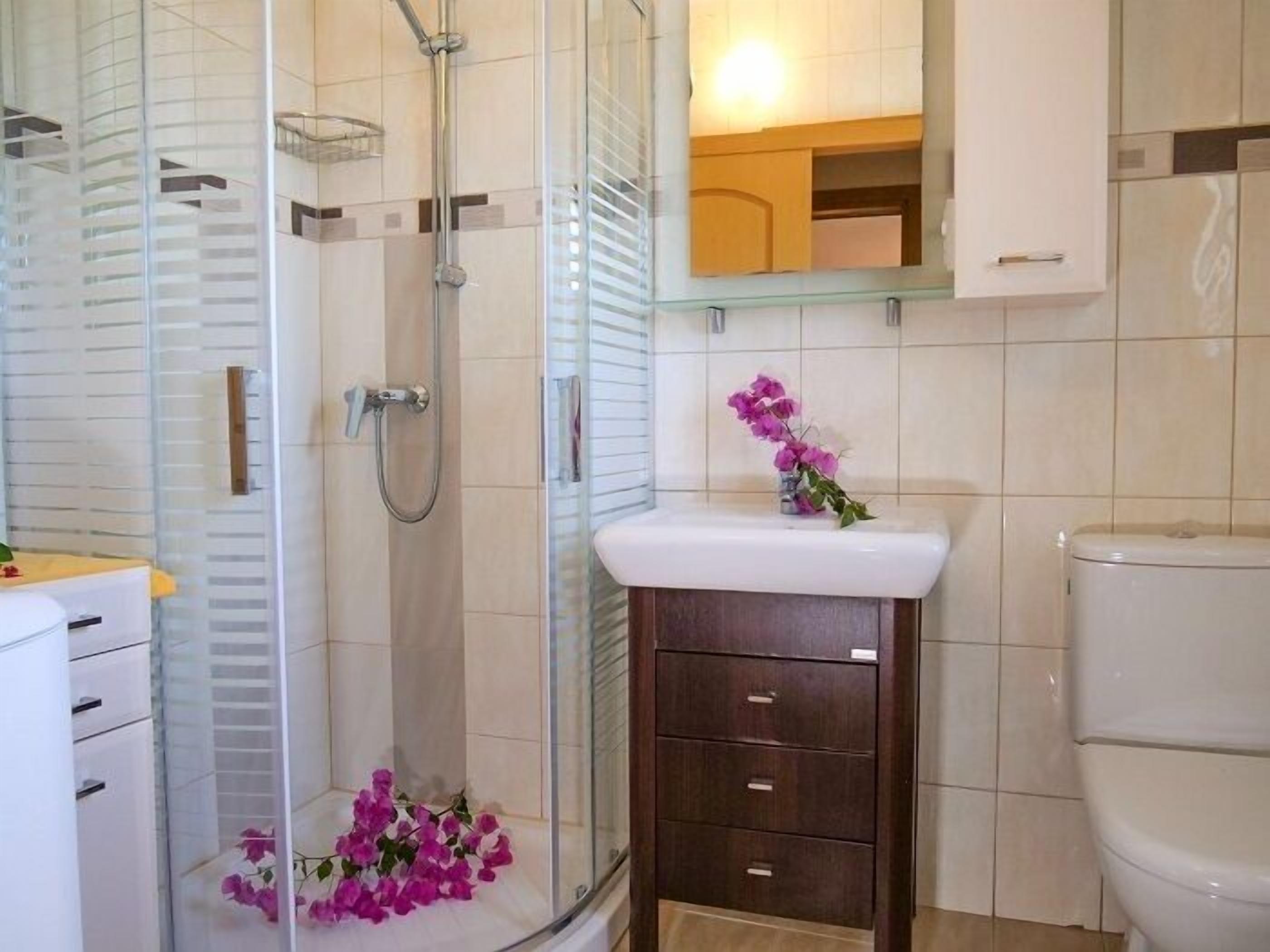 Een badkamer met een glazen douchecabine, een wit wastafelmeubel met een donker kastje, en een toilet.