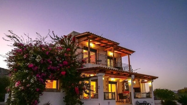 A two-story house with a balcony, a swimming pool, and a garden with pink flowers. - Villa Lindos Star in Rodos with pool (Rhodes)