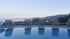 A poolside area with lounge chairs and a view of the sea and hills. - Villa Lindos Star in Rodos with pool (Rhodes)