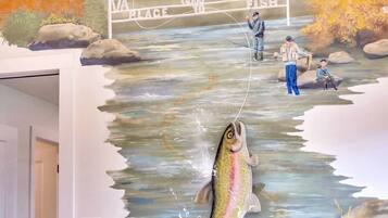 A mural of a river with people fishing, a sign that says "A TENNIS GOOD PLACE TO FISH," and a door to a room.
