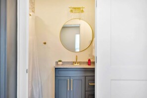 Un baño con un espejo redondo, un grifo dorado y un tocador azul.