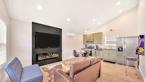 A modern living room with a flat-screen TV, a fireplace, a sofa, and a dining area.