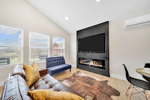 A modern living room with a leather sofa, a blue armchair, a fireplace, and a large TV mounted on the wall.