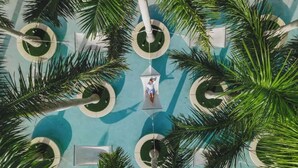 Vue aérienne d’un espace piscine agrémenté de palmiers, de zones de détente circulaires et d’une fontaine centrale.