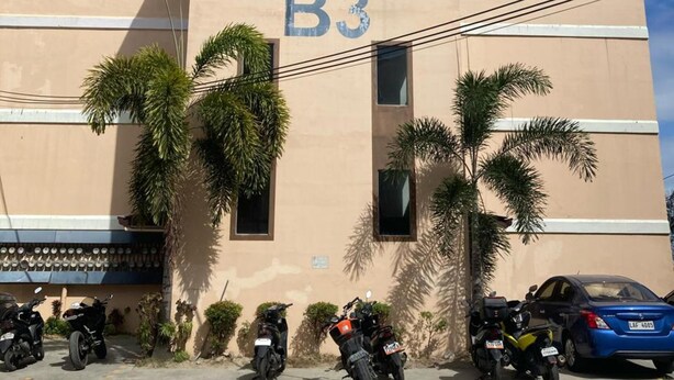 A building with the number B3 on its facade, surrounded by parked motorcycles and a blue car.