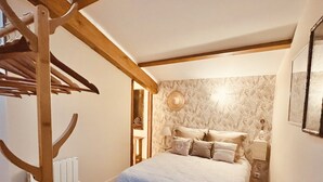 A bedroom with a bed, a wooden chair, a nightstand, and a wall-mounted lamp. - Charming Gîte in the Heart of Beaujolais (Lancié)