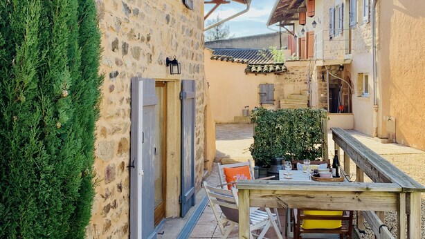 A stone building with a wooden table and chairs outside, surrounded by greenery and gravel. - Charming Gîte in the Heart of Beaujolais (Lancié)