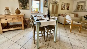 A dining area with a table set for four, surrounded by chairs. There is a cabinet with drawers, a wicker basket, and a vase with dried flowers on the table. - Charming Gîte in the Heart of Beaujolais (Lancié)