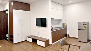 A modern kitchen with white cabinets, a built-in oven, a refrigerator, and a wooden bench. - Au79 Hotel & Apartment (Hai Phong)