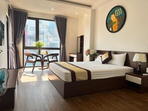 A hotel room with a large bed, a desk with a chair, a window with curtains, and a painting on the wall. - Au79 Hotel & Apartment (Hai Phong)