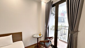 A hotel room with a bed, a small table with a chair, and a view of the outside balcony. - Au79 Hotel & Apartment (Hai Phong)