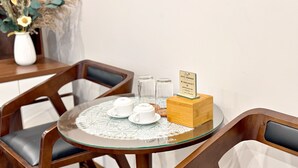 A round glass table with a white doily, two white teacups, a wooden block with a hotel sign, and a vase with dried flowers. - Au79 Hotel & Apartment (Hai Phong)