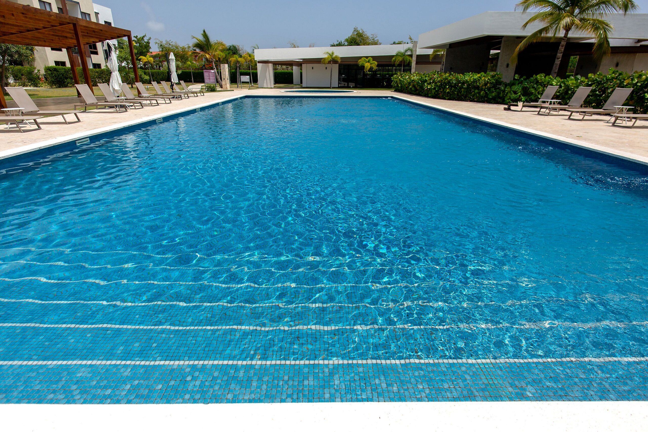 Una piscina rettangolare con acqua cristallina e azzurra, circondata da lettini e ombrelloni.