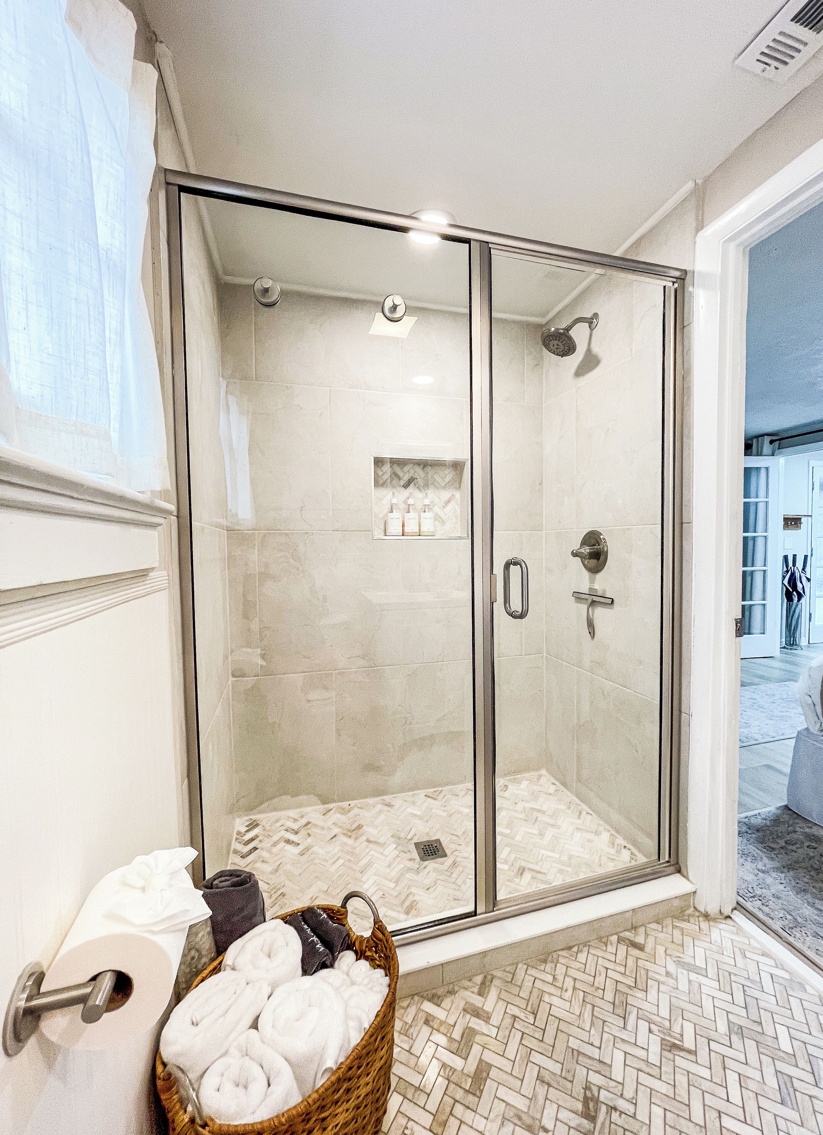 Un baño moderno con ducha acristalada, suelo de madera y una cesta de toallas.