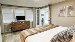 A bedroom with a bed, a dresser, a television, and a door leading to another room. - Sweet Magnolia, 3Br/2.5Ba, Downtown Historic Charm w/ all the comforts!  (Orlando)