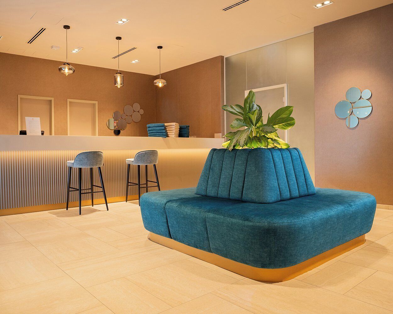 A reception area with a blue sofa, two bar stools, a reception desk, and a potted plant.
