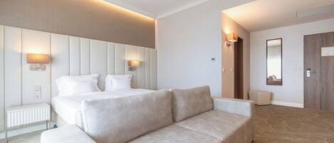 A modern hotel room with a large bed, two bedside lamps, a sofa, and a mirror.