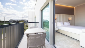 Un balcone con tavolo e sedie, un letto con biancheria da letto bianca e vista su uno stadio.